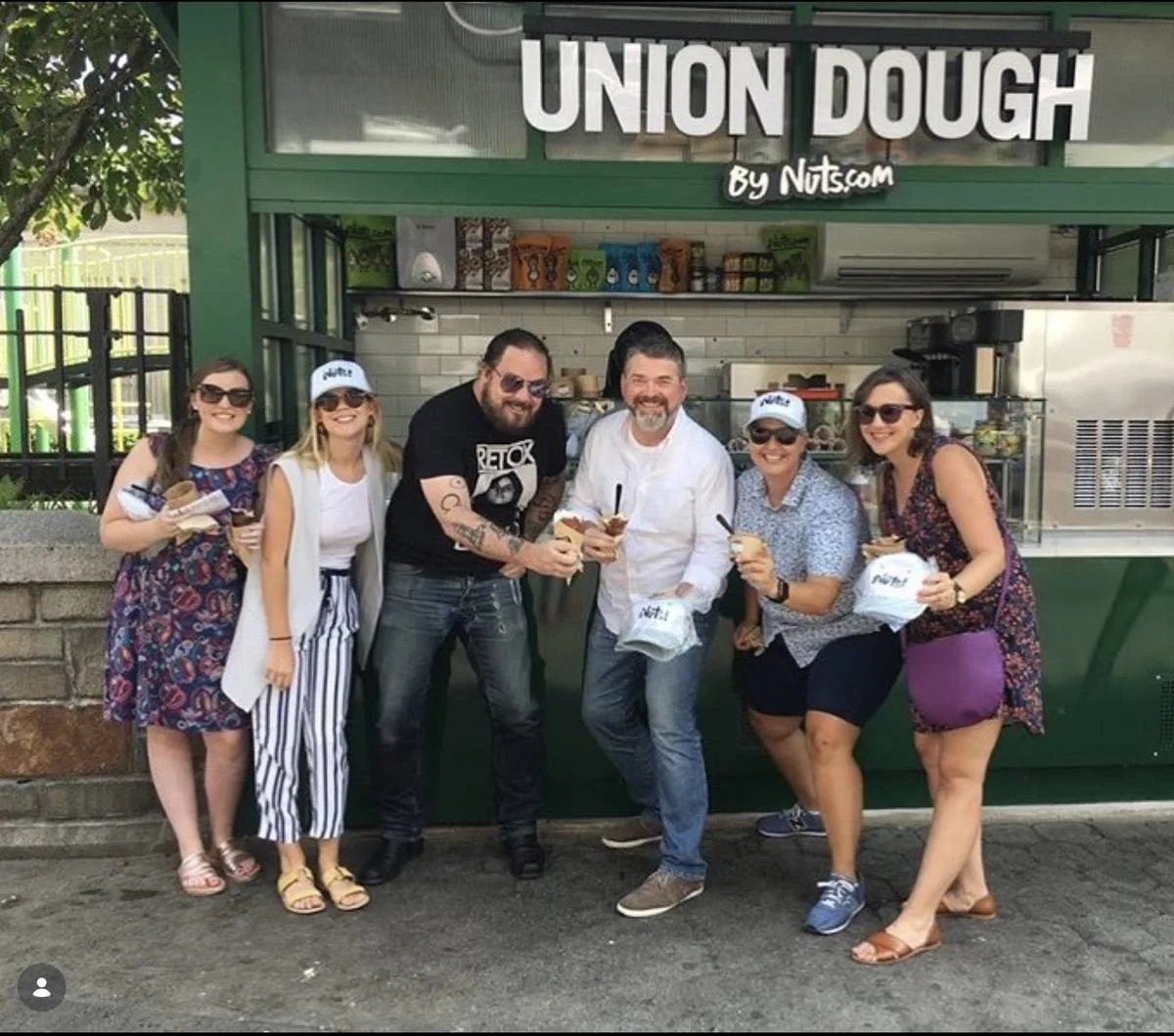Six people holding ice cream sandwiches outside a green kiosk signed Union Dough by Nuts.com